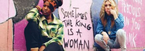 two women sitting next to a wall that says "Sometimes the king is a woman"