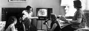 a black and white photo of people sitting in a living room watching TV