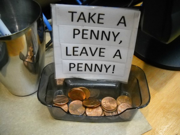 a cup of pennies with a sign 