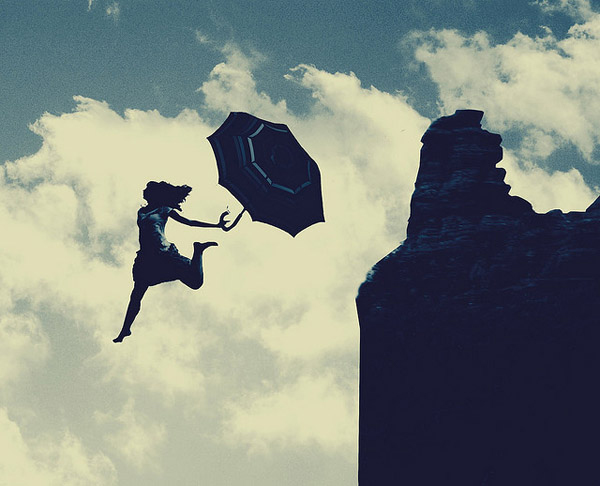 a women jumping off a cliff with an open umbrella in her hand