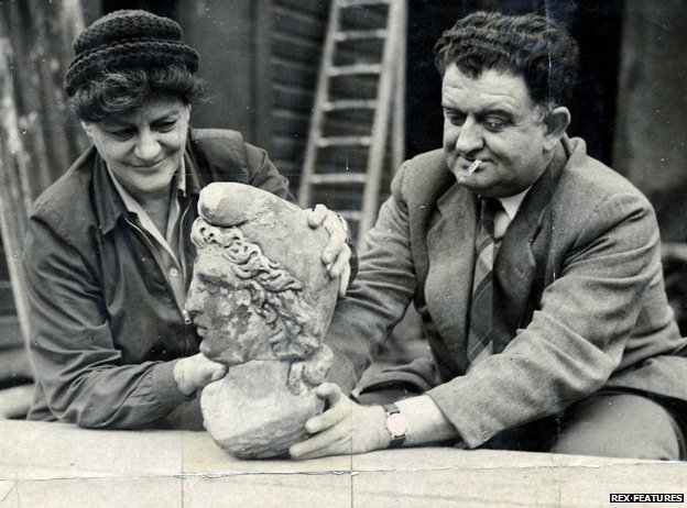 A black and white photo of a man and a women holding a sculpture of a woman